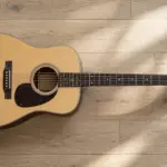Acoustic guitar seen from above on a wooden floor showing headstock and tuning pegs