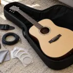 Open gig bag with strap, cable, cloth and strings beside an acoustic guitar